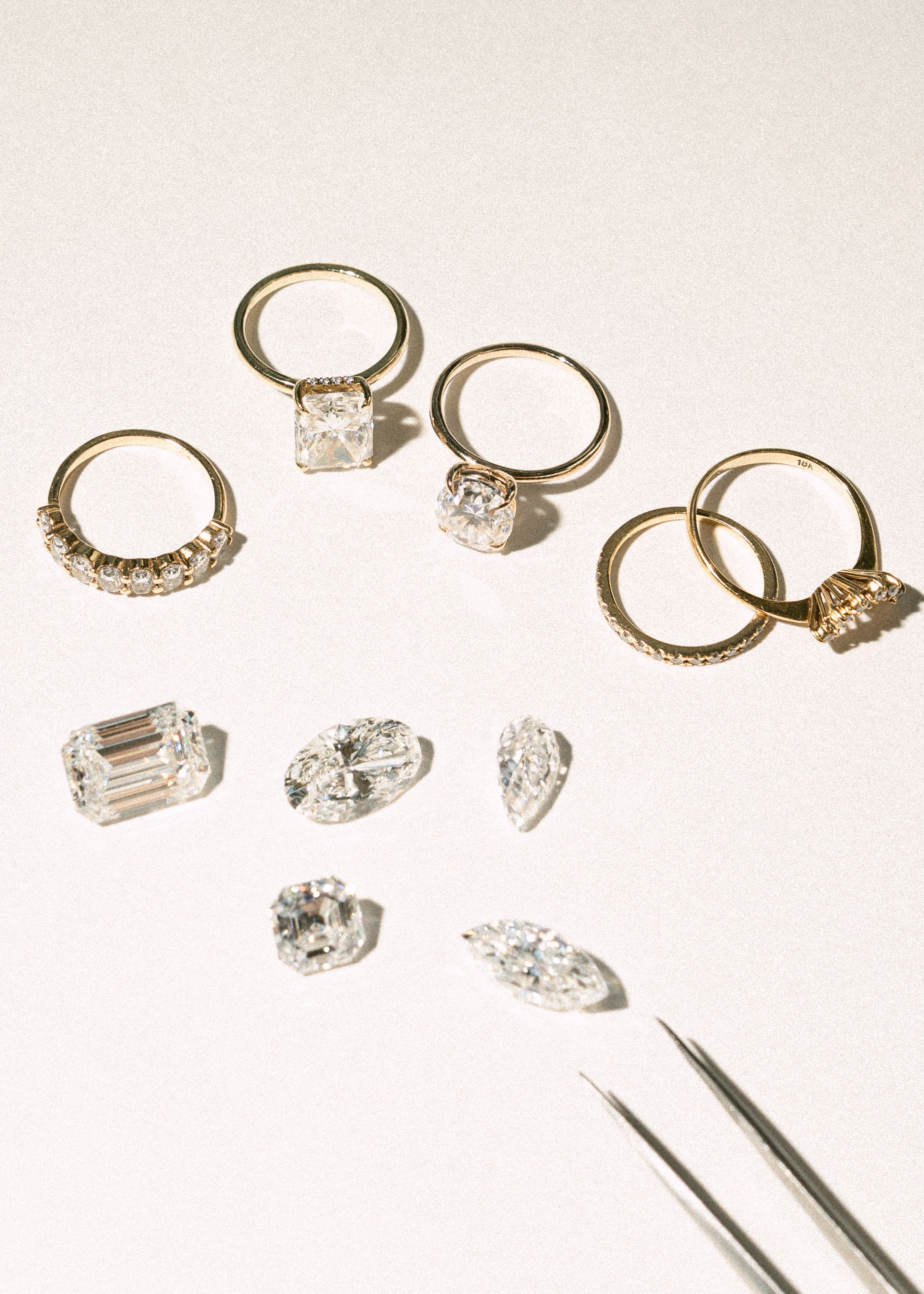 Gold engagement rings and loose diamonds arranged on a cream surface